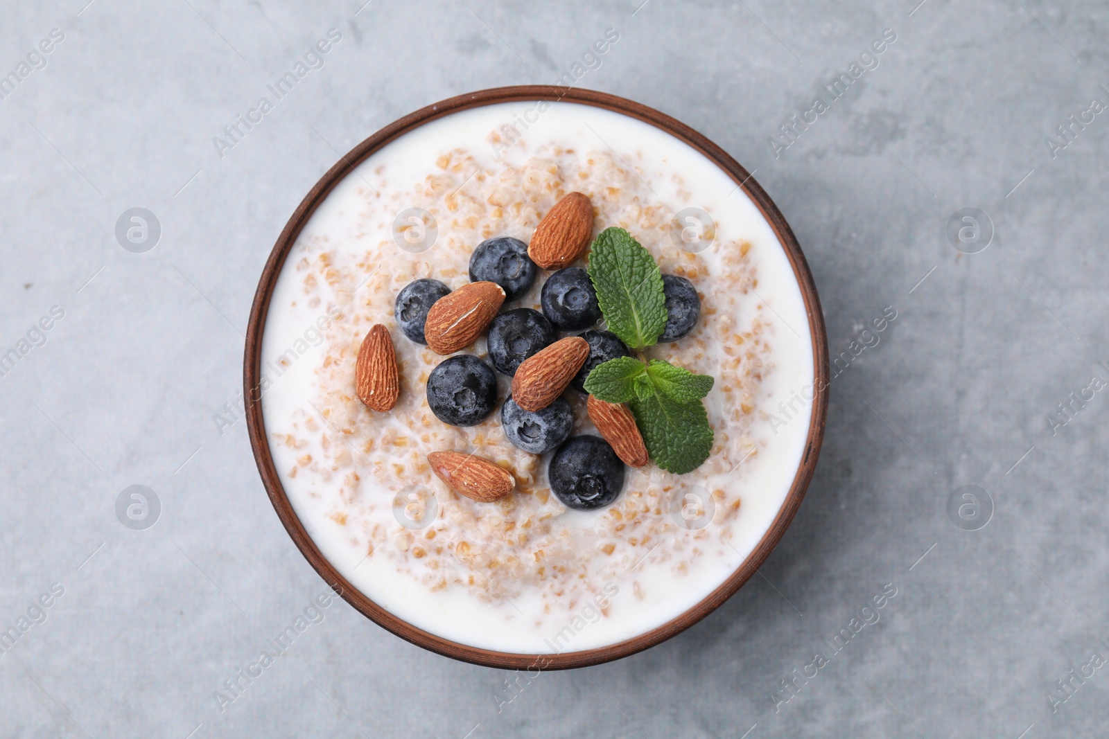 Photo of Tasty wheat porridge with milk, blueberries and almonds in bowl on gray table, top view