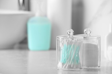 Photo of Containers with cotton swabs and pads on white countertop in bathroom. Space for text