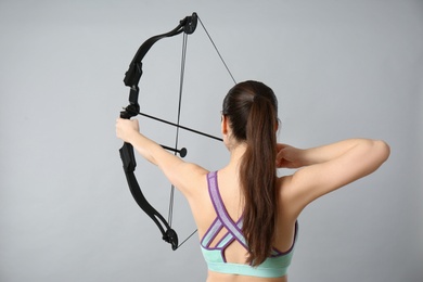 Young woman practicing archery on light grey background, back view