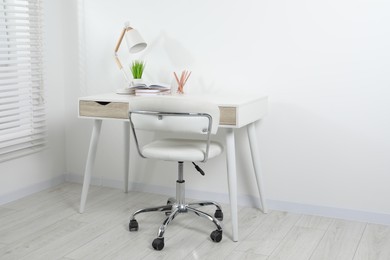Comfortable workplace with white desk near wall indoors