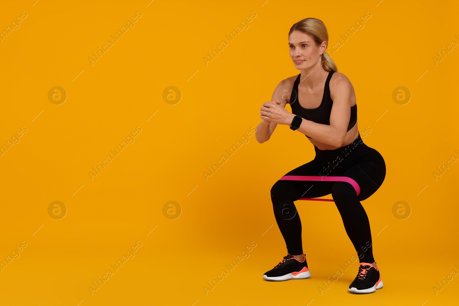 Photo of Woman exercising with elastic resistance band on orange background. Space for text