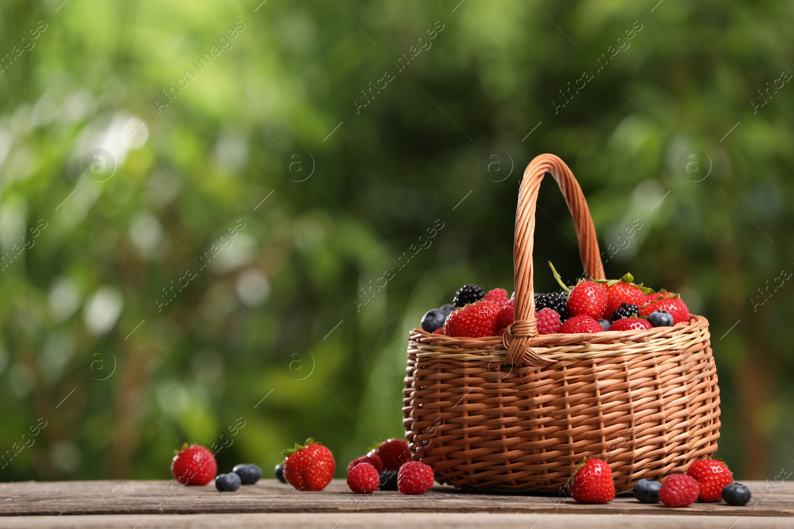 Photo of Wicker basket with different fresh ripe berries on wooden table outdoors, space for text