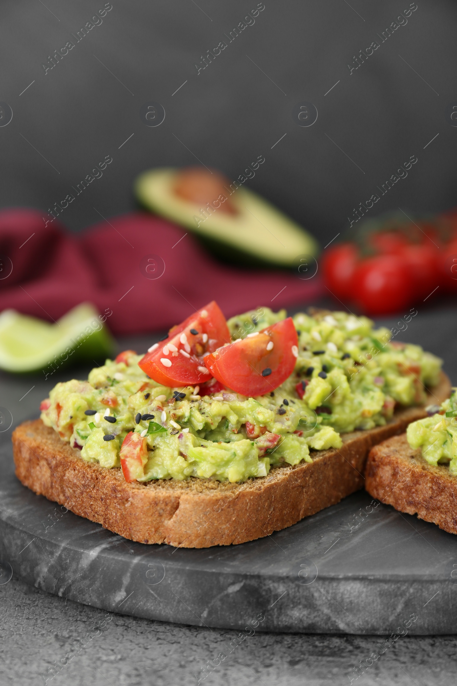 Photo of Slices of bread with tasty guacamole and ingredients on grey table, closeup