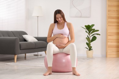 Photo of Pregnant woman sitting on fitness ball at home. Doing yoga