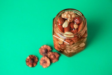 Photo of Jar with different tasty nuts and honey on green background, above view