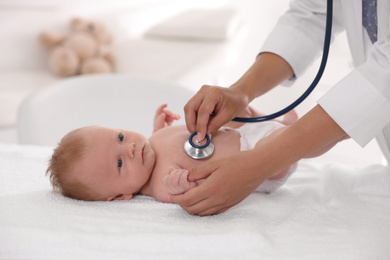 Photo of Doctor examining cute baby with stethoscope indoors, closeup. Health care