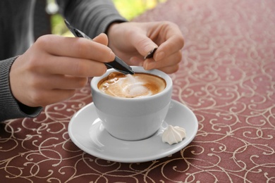 Young woman adding sugar to delicious coffee at table