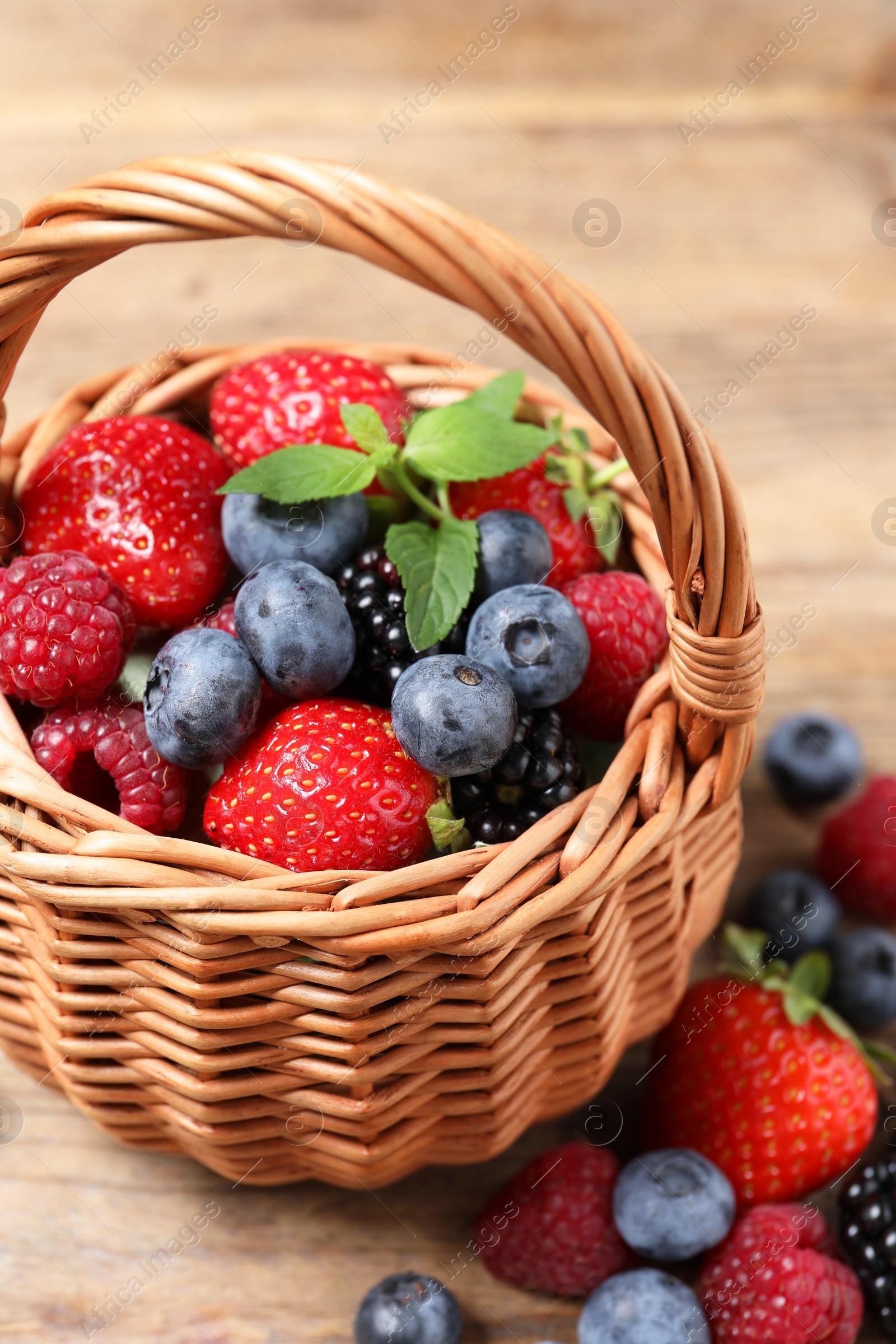 Photo of Wicker basket with many different fresh ripe berries on wooden table, closeup