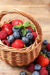 Wicker basket with many different fresh ripe berries on wooden table, closeup