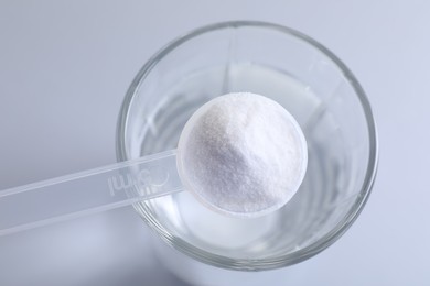 Spoon with baking soda over glass of water on light grey background, top view