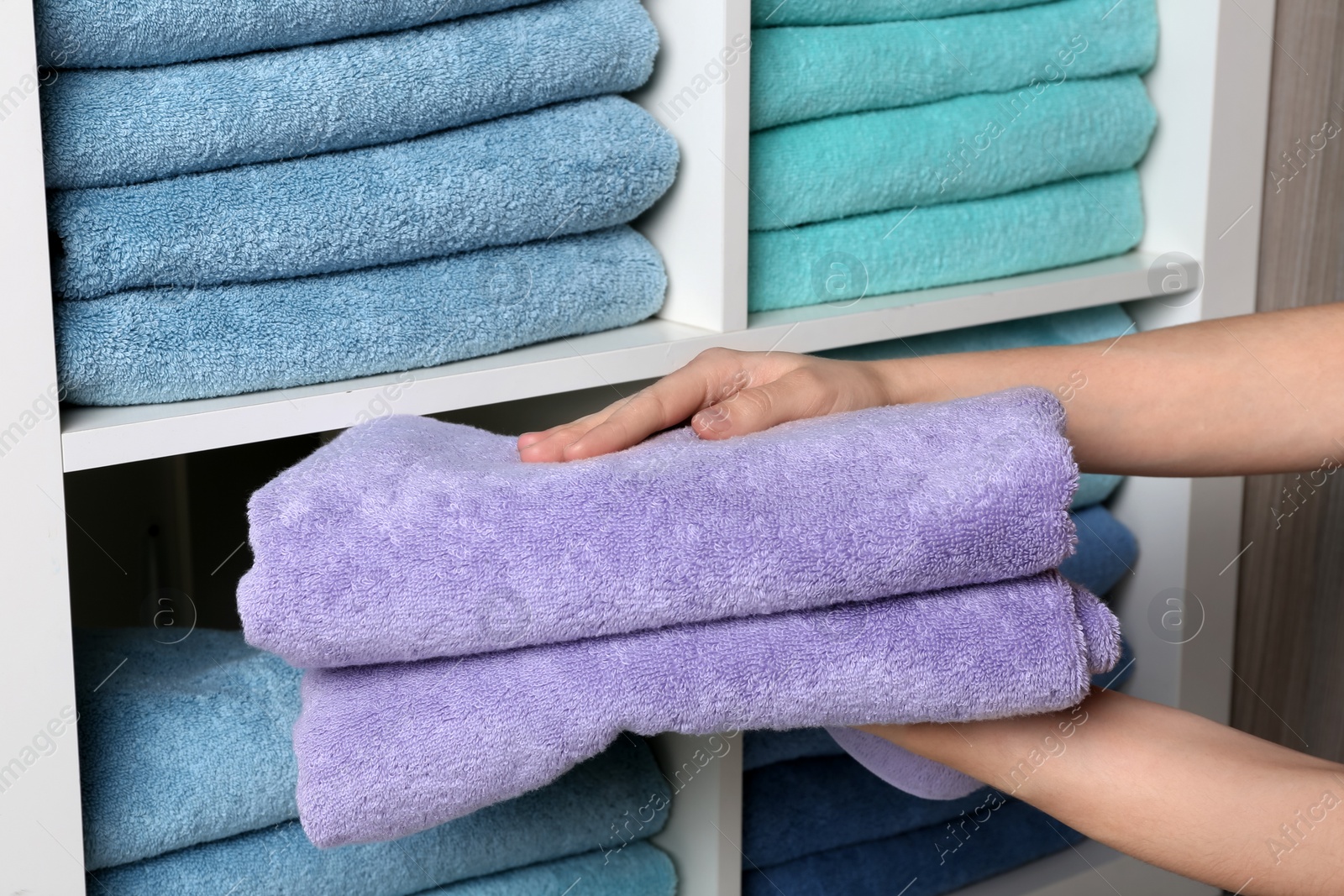 Photo of Woman putting towels on shelf, closeup view