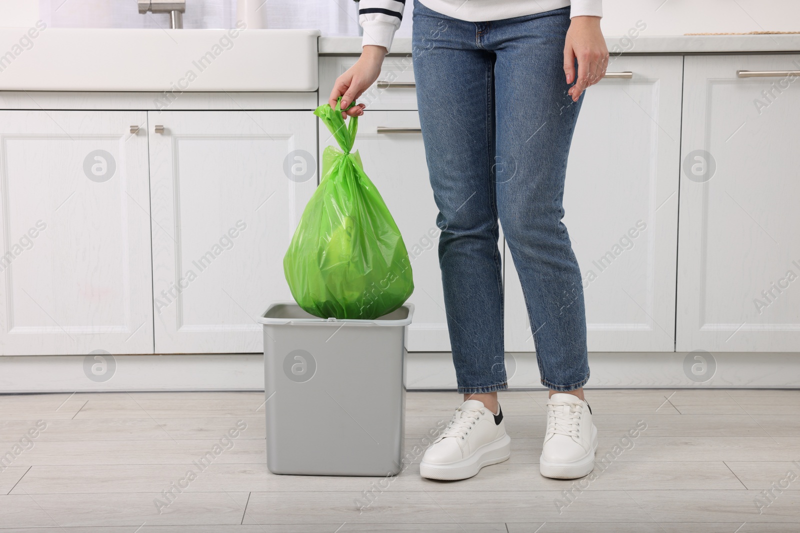 Photo of Woman taking garbage bag out of trash bin in kitchen, closeup