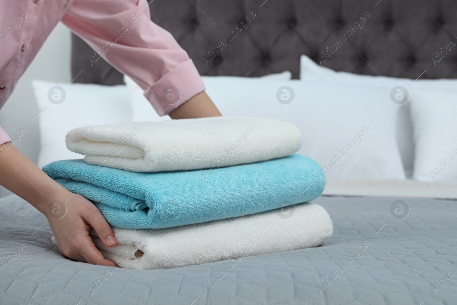 Photo of Woman putting stack of clean towels on bed