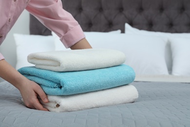 Photo of Woman putting stack of clean towels on bed