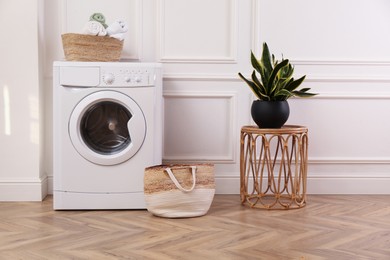 Photo of Laundry room interior with modern washing machine and beautiful houseplant near white wall