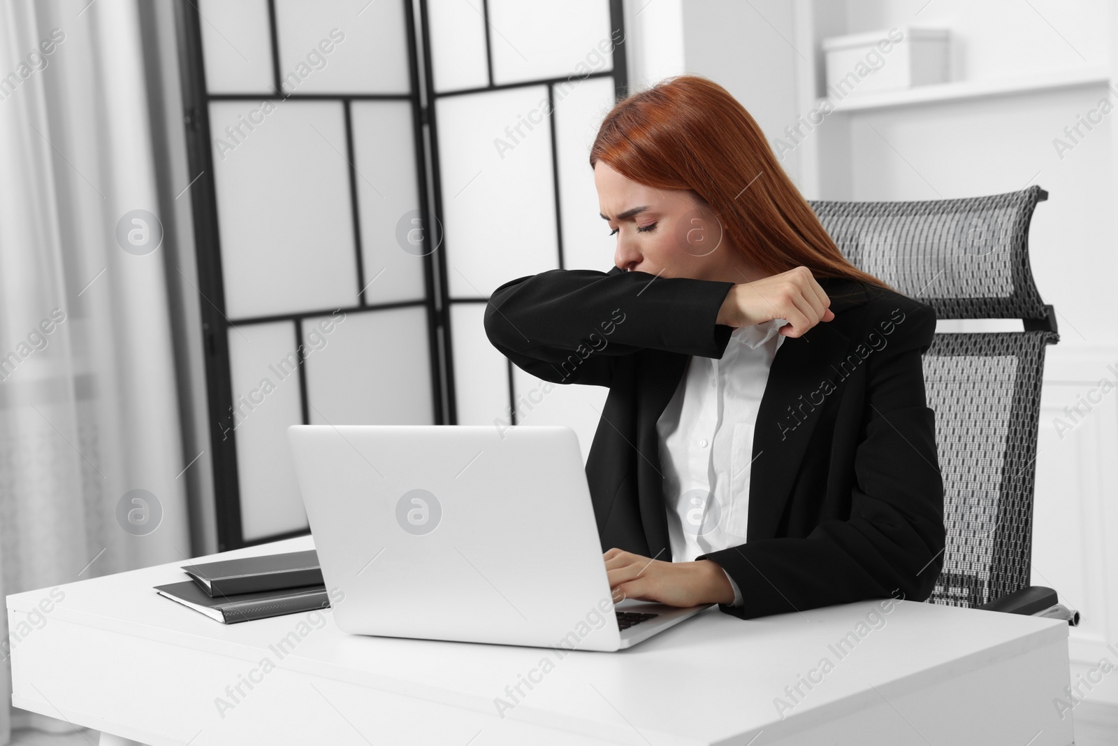 Photo of Woman coughing while using laptop at table in office. Cold symptoms