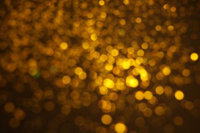 Blurred view of golden glitter on dark background. Bokeh effect