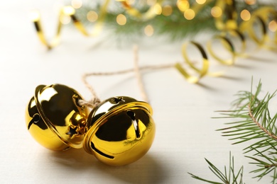 Photo of Golden sleigh bells and fir branch on white table, closeup