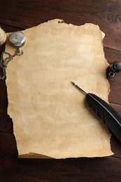 Photo of Sheet of old parchment paper, black feather, inkwell and pocket chain clock on wooden table, flat lay