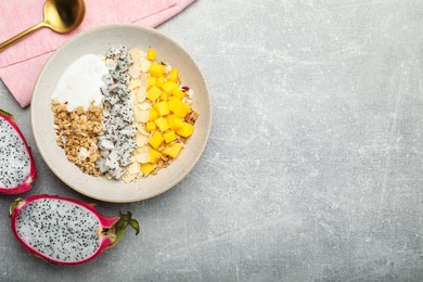 Photo of Bowl of granola with pitahaya, mango and yogurt served on light grey table, flat lay. Space for text