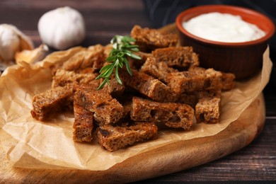 Photo of Crispy rusks with rosemary and sauce on wooden table, closeup