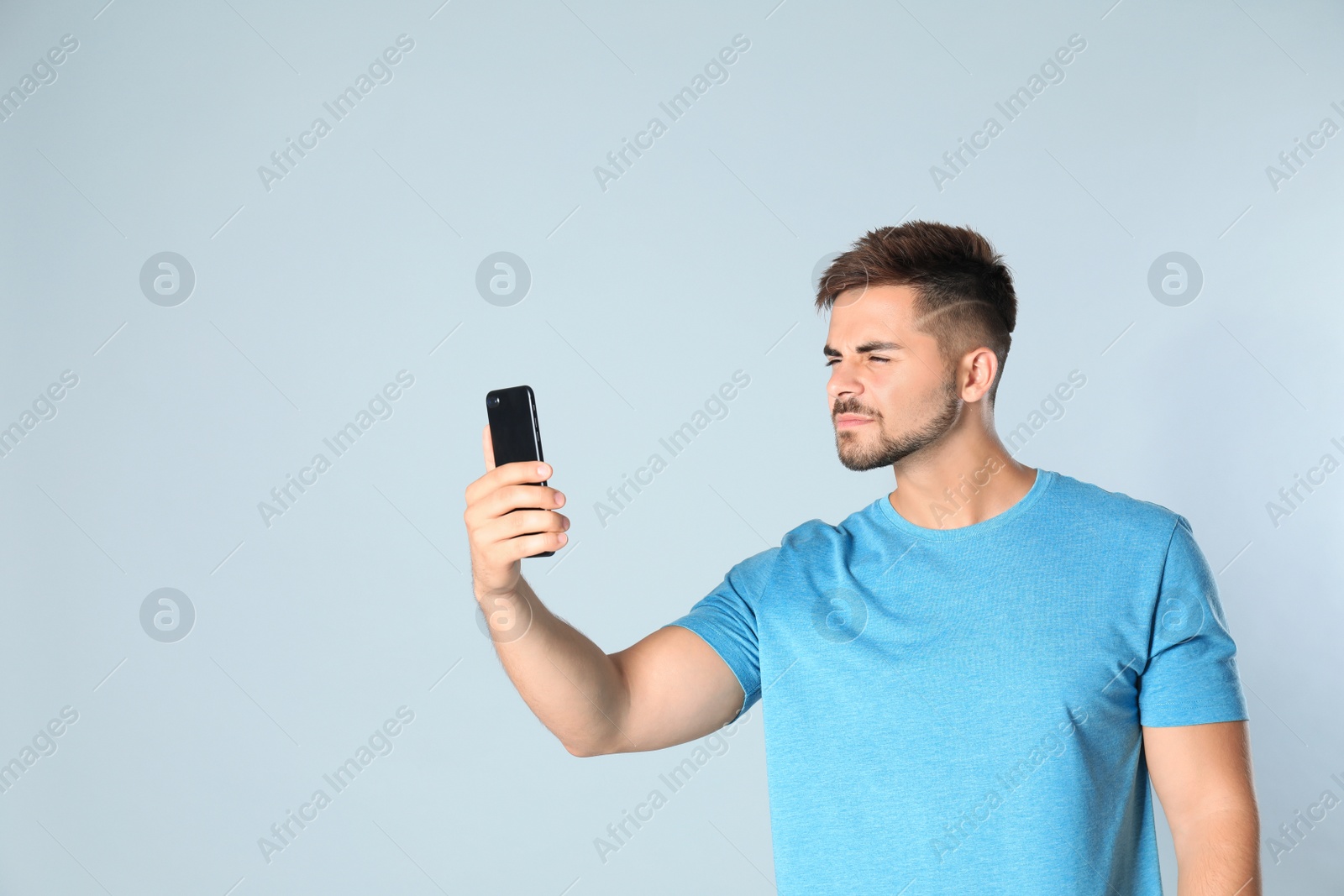 Photo of Young man with vision problems using smartphone on grey background, space for text