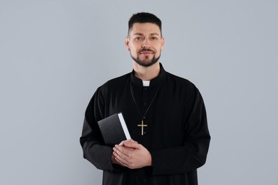 Priest with Bible and cross on grey background