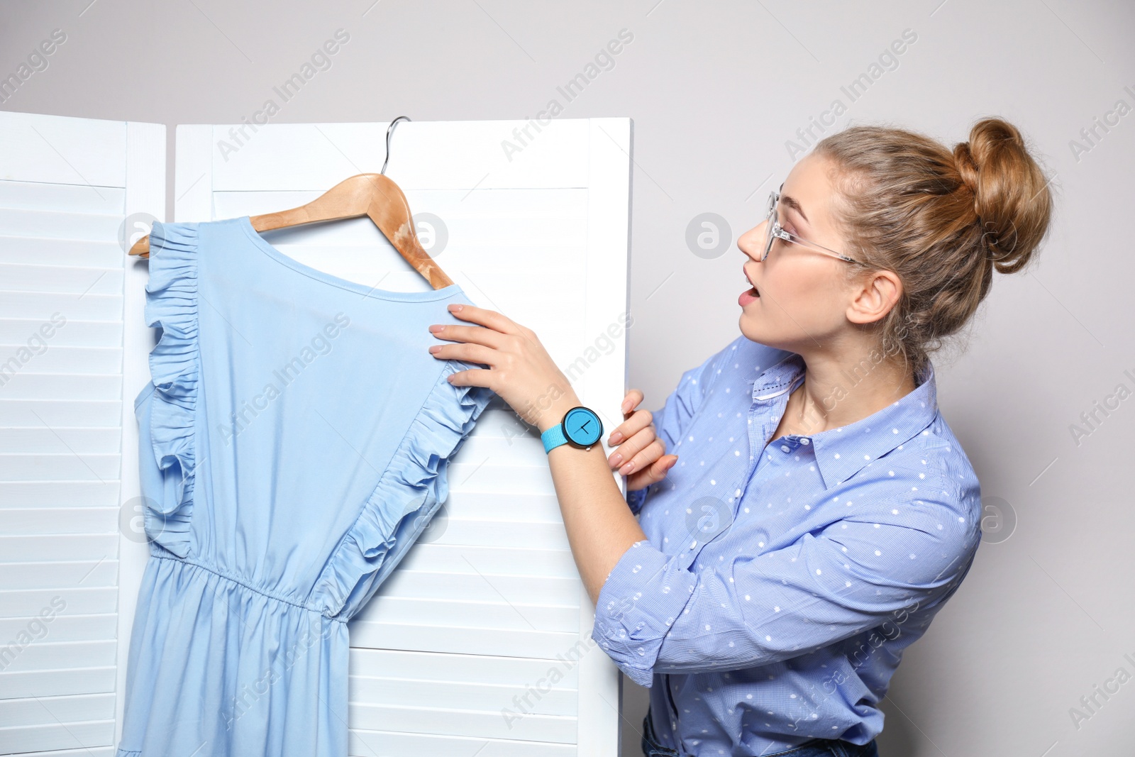 Photo of Young woman with clothes on hanger near folding screen against light background. Dressing room