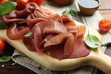 Board with delicious bresaola served with tomato and basil leaves on wooden table, closeup