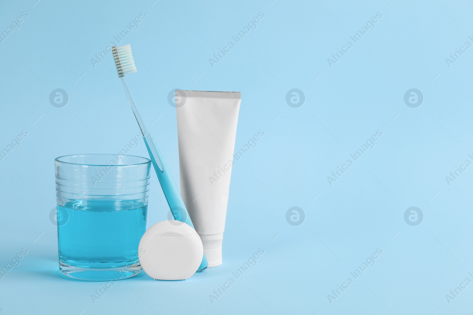 Photo of Mouthwash, toothbrush, paste and dental floss on light blue background, space for text