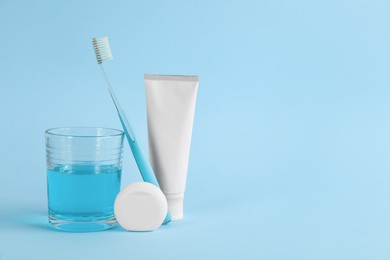 Photo of Mouthwash, toothbrush, paste and dental floss on light blue background, space for text
