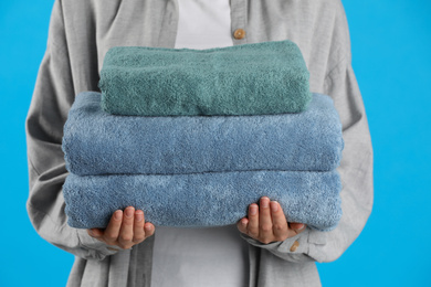 Photo of Woman holding fresh towels on light blue background, closeup