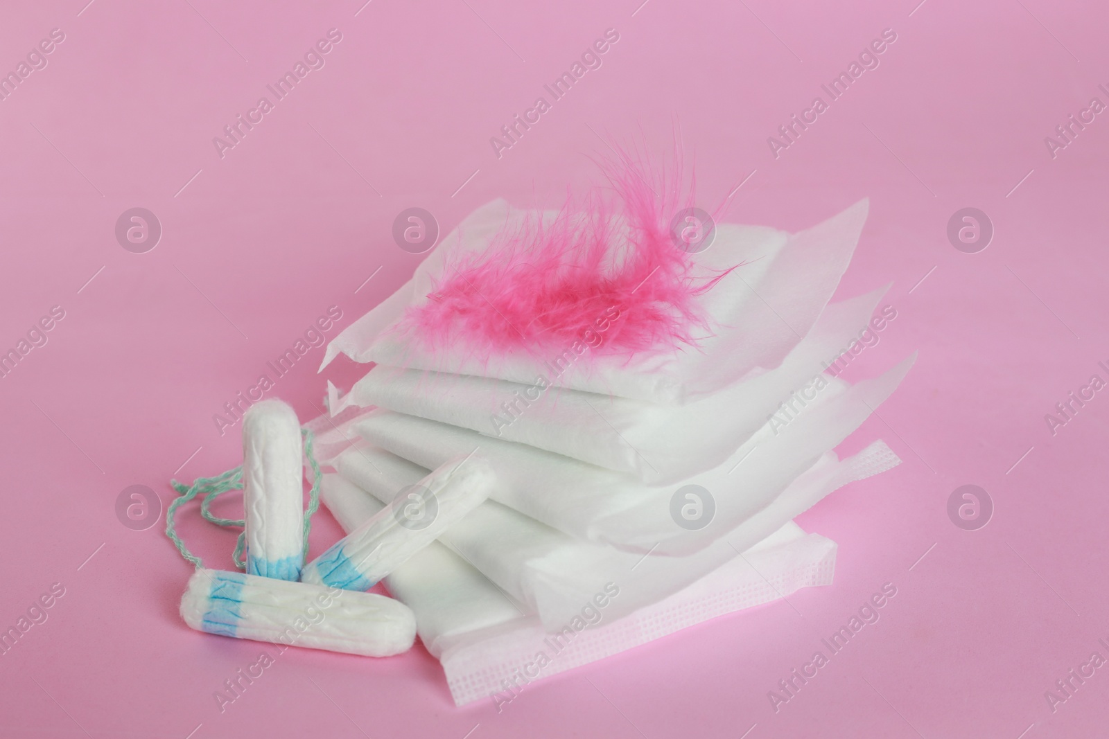 Photo of Menstrual pads with feather and tampons on pink background