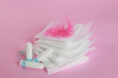 Photo of Menstrual pads with feather and tampons on pink background