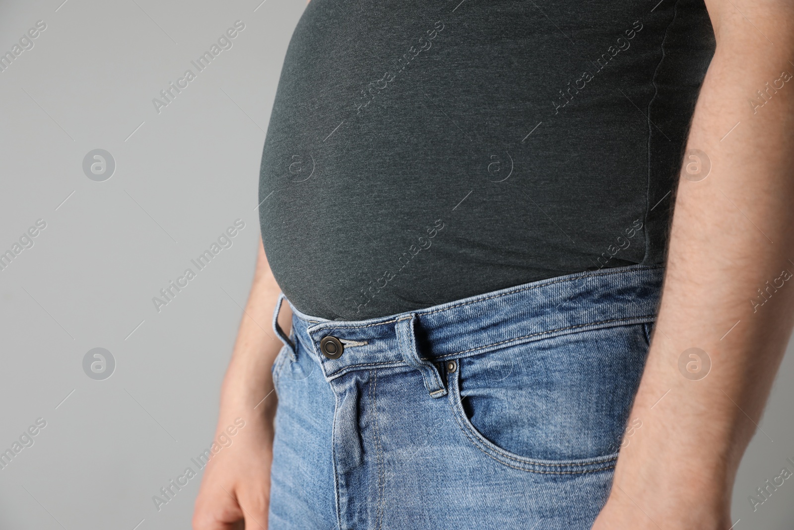 Photo of Overweight man in tight tshirt and jeans on light grey background, closeup. Space for text