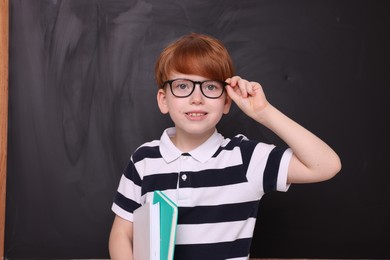 Photo of Cute schoolboy in glasses with books near blackboard
