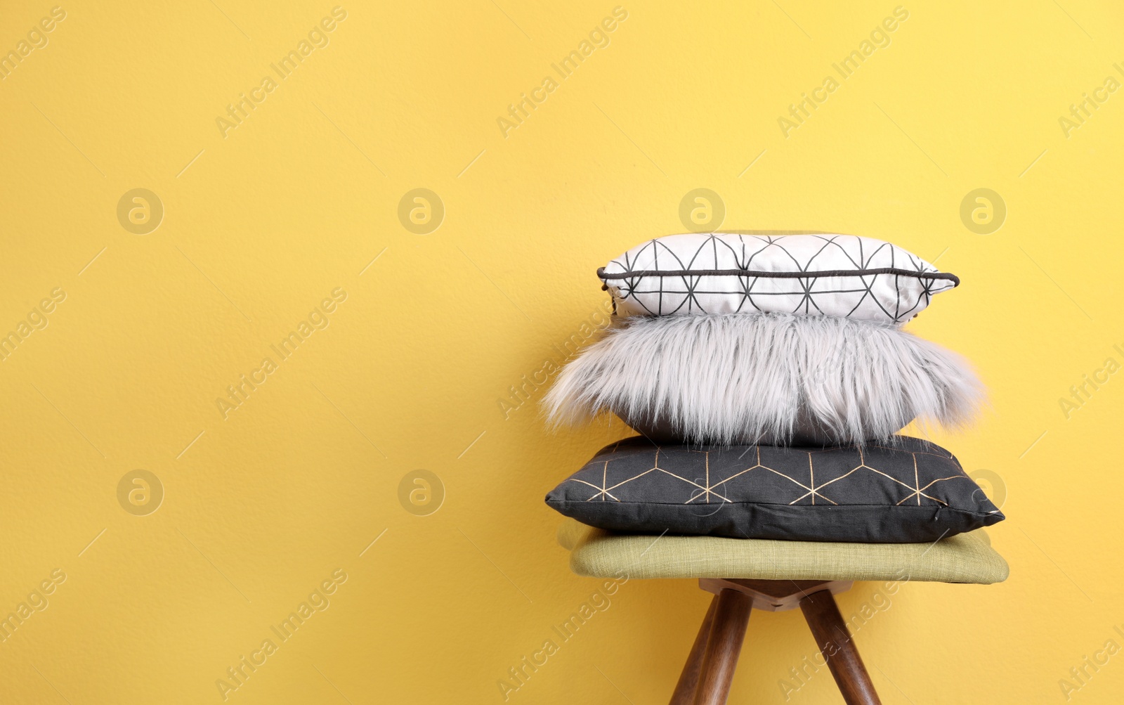 Photo of Many different pillows on chair near color wall with space for text