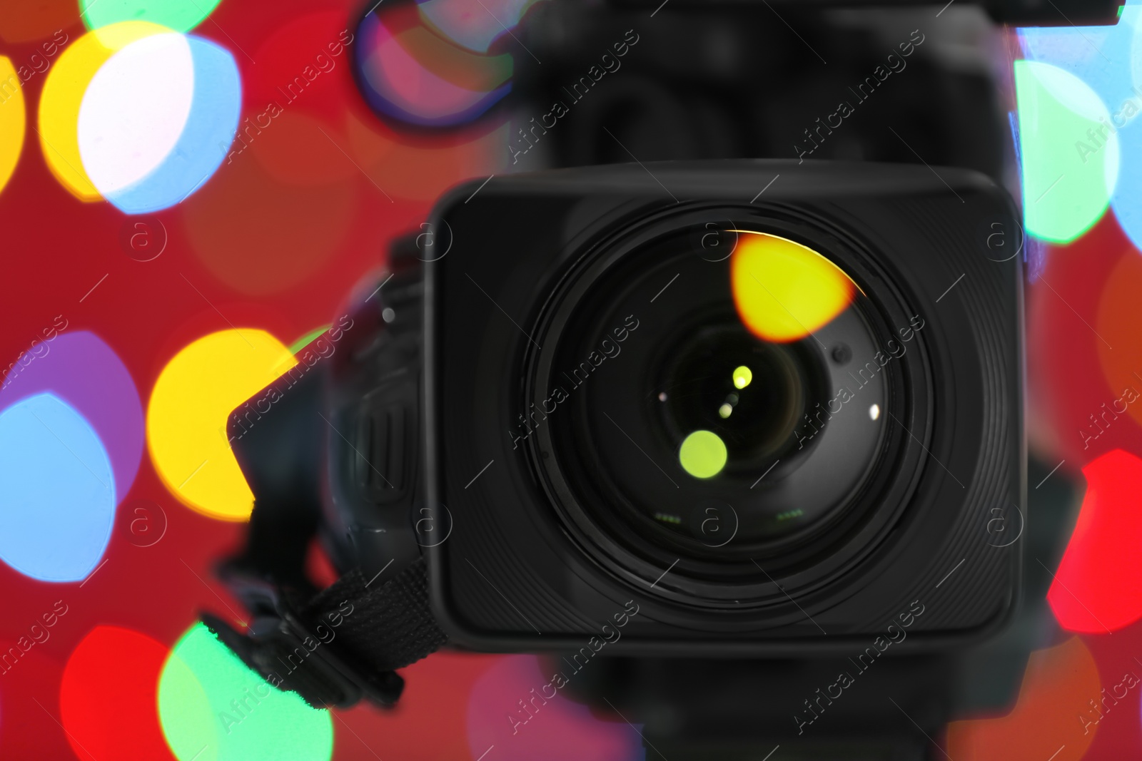 Photo of Modern video camera against blurred colorful lights, closeup