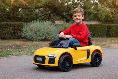 Photo of Cute little boy driving children's car outdoors