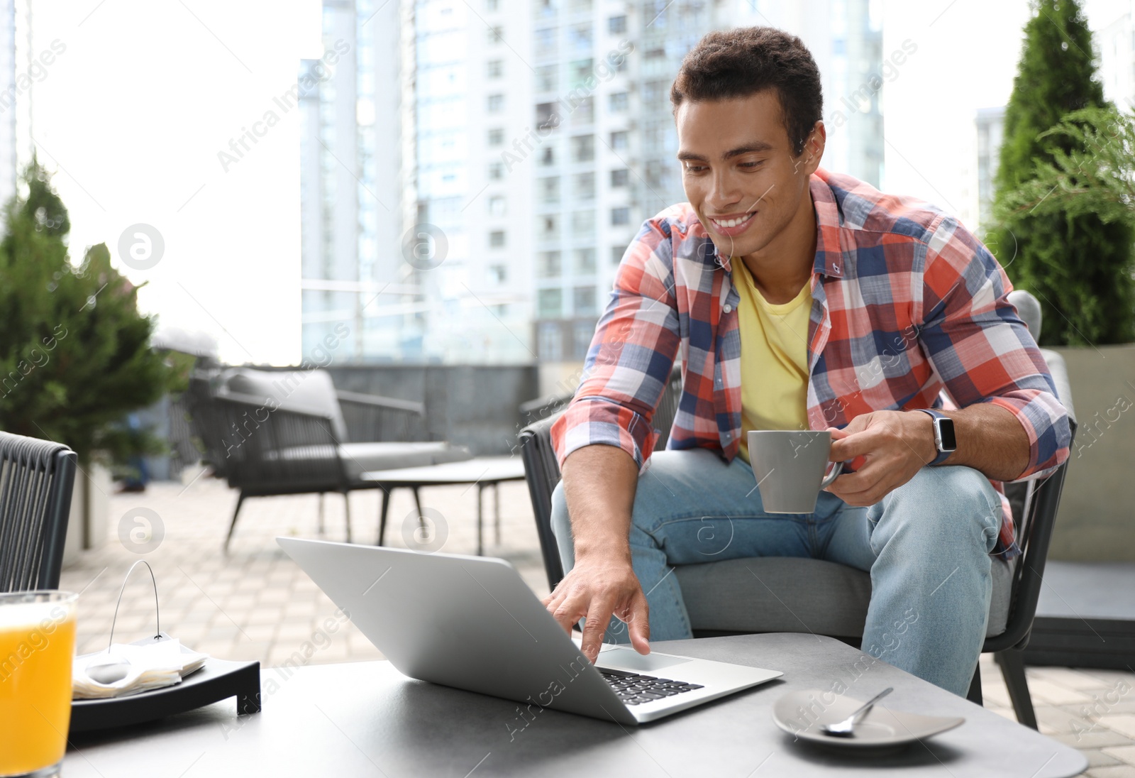 Photo of Portrait of handsome young African-American man with laptop and cup of drink in outdoor cafe