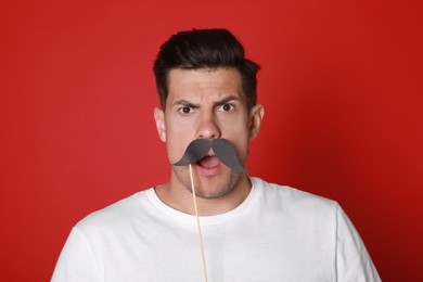 Emotional man with fake mustache on red background