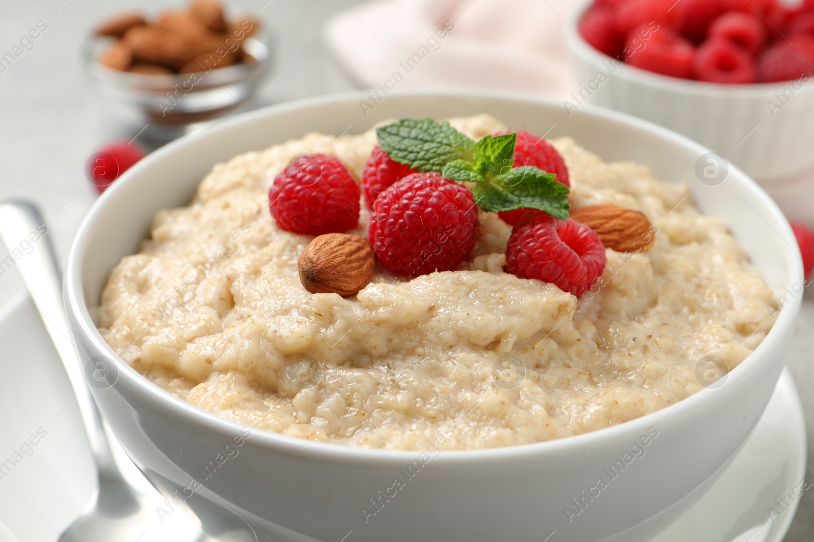 Photo of Tasty oatmeal porridge with raspberries and almond nuts in bowl on table, closeup