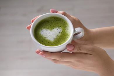 Photo of Woman with cup of delicious matcha latte on light grey background, closeup