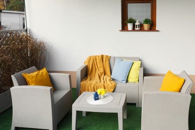 Beautiful rattan garden furniture, soft pillows, blanket and yellow chrysanthemum flowers outdoors
