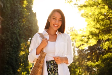 Young woman with stylish straw bag in park