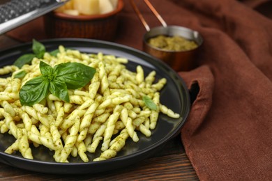 Photo of Plate of delicious trofie pasta with pesto sauce and basil leaves on wooden table, closeup. Space for text