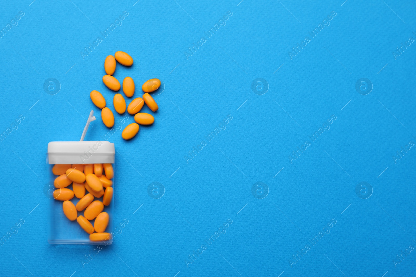 Photo of Tasty orange dragee candies and container on blue background, flat lay. Space for text