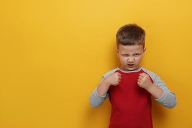 Photo of Angry little boy on yellow background, space for text. Aggressive behavior