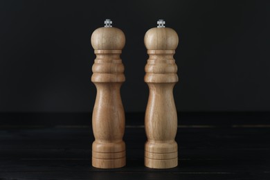 Photo of Salt and pepper shakers on black wooden table, closeup