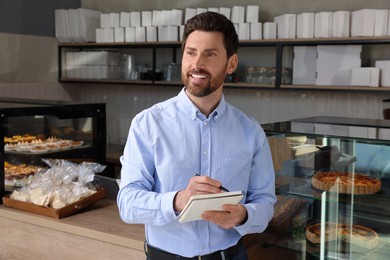 Photo of Happy business owner with notebook and pen in bakery shop